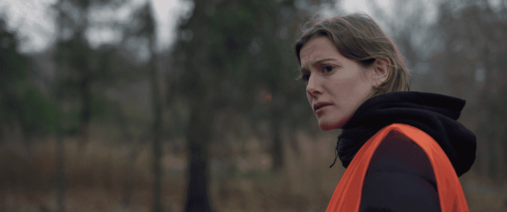 a young woman wearing an orange vest looks worryingly off camera